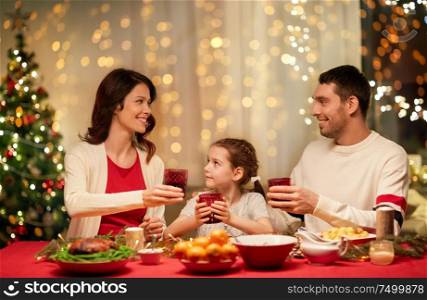 holidays, family and celebration concept - happy mother, father and little daughter having christmas dinner at home. happy family having christmas dinner at home