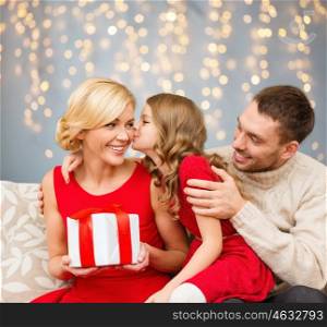 holidays, family and people concept - happy girl kissing her mother with christmas gift over lights background