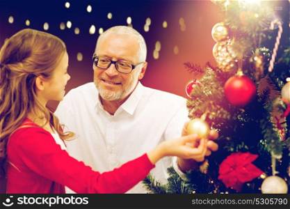 holidays, family and people concept - happy grandfather and granddaughter decorating christmas tree over lights background. happy family decorating christmas tree