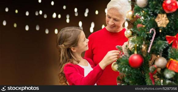 holidays, family and people concept - happy grandmother and granddaughter decorating christmas tree over lights background. happy family decorating christmas tree