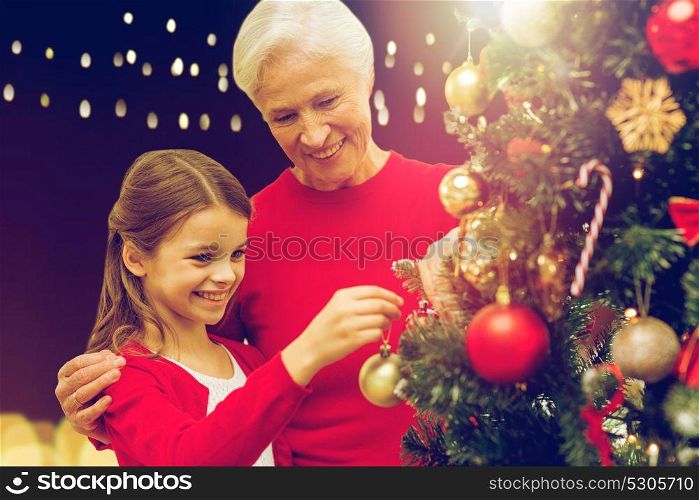 holidays, family and people concept - happy grandmother and granddaughter decorating christmas tree over lights background. happy family decorating christmas tree