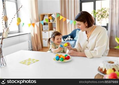 holidays, family and people concept - happy little baby daughter and mother tapping colored easter eggs at home. baby girl and mother tapping easter eggs at home
