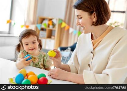 holidays, family and people concept - happy little baby daughter and mother tapping colored easter eggs at home. baby girl and mother tapping easter eggs at home