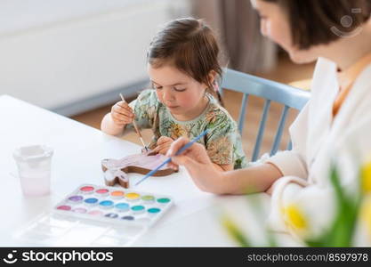 holidays, family and people concept - happy mother and little baby daughter coloring easter bunny with watercolors at home. mother with child coloring easter bunny at home