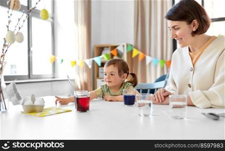holidays, family and people concept - happy mother and little baby daughter dyeing easter eggs with colors at home. mother with child dyeing easter eggs at home