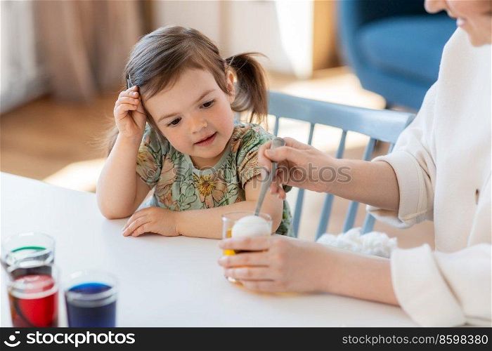 holidays, family and people concept - happy mother and little baby daughter dyeing easter eggs with colors at home. mother with child dyeing easter eggs at home