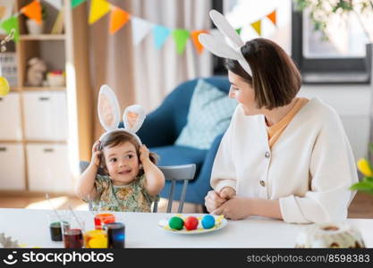 holidays, family and people concept - happy mother and little baby daughter in bunny ears dyeing easter eggs at home. mother with child dyeing easter eggs at home