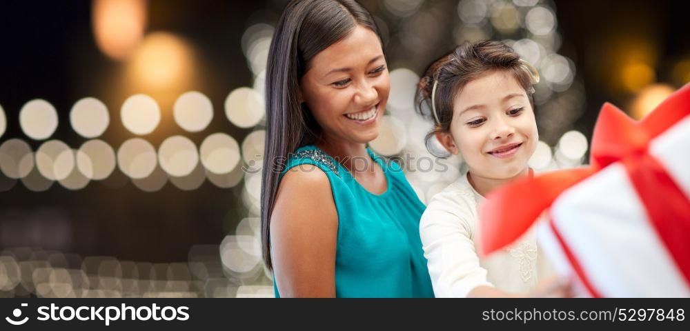 holidays, family and people concept - happy mother and little daughter with gift box over christmas lights background. happy mother and daughter with christmas gift