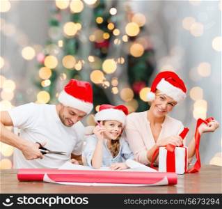 holidays, family and people concept - happy mother, father and little girl in santa helper hats with gift box and scissors over christmas tree lights background