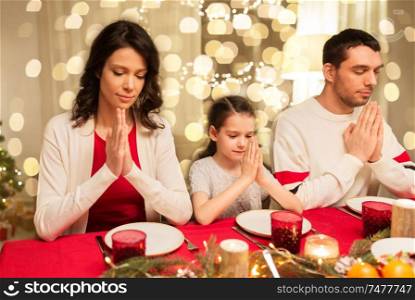 holidays, family and thankfulness concept - happy mother, father and little daughter having christmas dinner and praying before meal at home. family praying before meal at christmas dinner