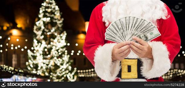 holidays, finances and people concept - close up of santa claus with dollar money over christmas tree background. close up of santa claus with dollar money