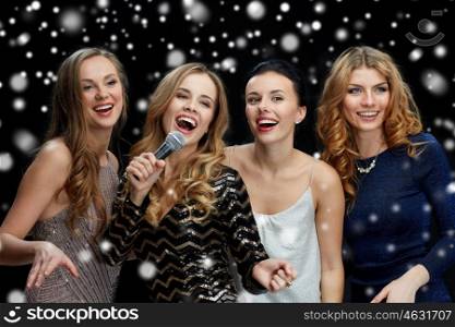 holidays, friends, bachelorette party, nightlife and people concept - three women in evening dresses with microphone singing karaoke over black background
