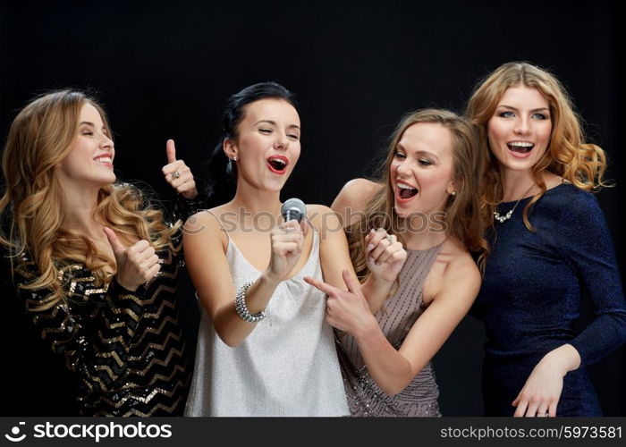 holidays, friends, bachelorette party, nightlife and people concept - three women in evening dresses with microphone singing karaoke over black background