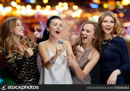 holidays, friends, bachelorette party, nightlife and people concept - three women in evening dresses with microphone singing karaoke over night club disco lights background