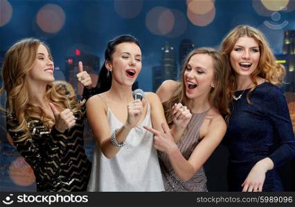 holidays, friends, bachelorette party, nightlife and people concept - three women in evening dresses with microphone singing karaoke over city and lights background