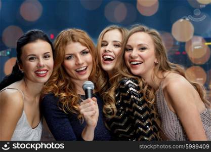 holidays, friends, bachelorette party, nightlife and people concept - three women in evening dresses with microphone singing karaoke over lights background