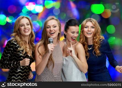 holidays, friends, bachelorette party, nightlife and people concept - three women in evening dresses with microphone singing karaoke over lights background