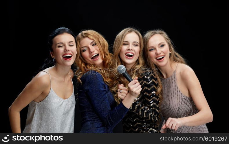 holidays, friends, bachelorette party, nightlife and people concept - three women in evening dresses with microphone singing karaoke over black background