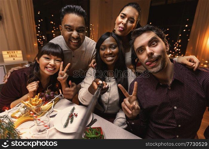 holidays, friendship and celebration concept - multiethnic group of happy friends having christmas dinner at home and taking selfie. friends taking selfie on christmas dinner at home