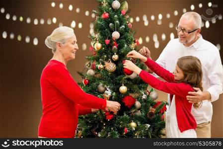 holidays, generation and people concept - happy family decorating christmas tree over lights background. happy family decorating christmas tree