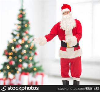 holidays, gesture and people concept - man in costume of santa claus over living room and christmas tree background
