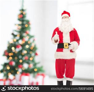 holidays, gesture and people concept- man in costume of santa claus showing thumbs up over living room and christmas tree background