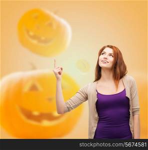 holidays, gesture and people concept - smiling teenage girl in casual clothes pointing finger up over halloween pumpkins background