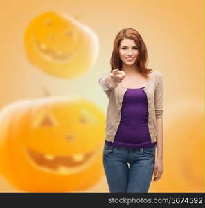 holidays, gesture and people concept - smiling teenage girl in casual clothes pointing finger on you over halloween pumpkins background