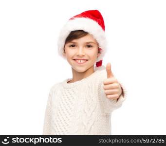 holidays, gesture, christmas, childhood and people concept - smiling happy boy in santa hat showing thumbs up