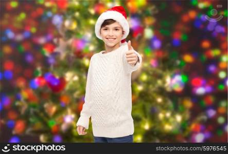 holidays, gesture, christmas, childhood and people concept - smiling happy boy in santa hat showing thumbs up over holidays lights background