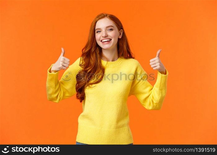 Holidays, gestures, people concept. Cheerful cute redhead girl smiling and showing thumbs-up recommend product, give positive reply, agree or like something, nod agreement, orange background.. Holidays, gestures, people concept. Cheerful cute redhead girl smiling and showing thumbs-up recommend product, give positive reply, agree or like something, nod agreement, orange background