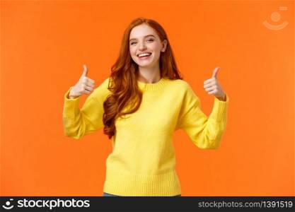 Holidays, gestures, people concept. Cheerful cute redhead girl smiling and showing thumbs-up recommend product, give positive reply, agree or like something, nod agreement, orange background.. Holidays, gestures, people concept. Cheerful cute redhead girl smiling and showing thumbs-up recommend product, give positive reply, agree or like something, nod agreement, orange background