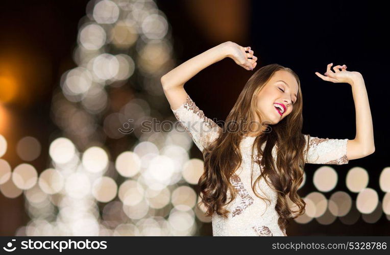 holidays, hairstyle and people concept - happy young woman or teen girl in fancy dress dancing over christmas tree lights background. happy young woman over christmas tree lights