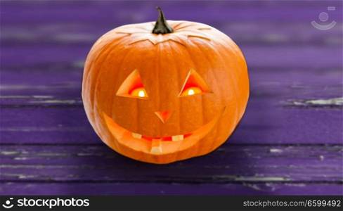 holidays, halloween and decoration concept - close up of carved pumpkin over ultra violet shabby boards background. close up of halloween pumpkin on table
