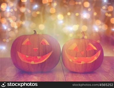 holidays, halloween and decoration concept - close up of carved pumpkins with smiley faces on table over lights
