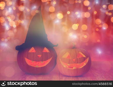 holidays, halloween and decoration concept - close up of carved pumpkins with smiley faces and witch hat on table over lights