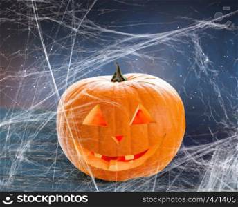 holidays, halloween and decoration concept - pumpkin or jack o lantern on table and spiderweb over starry night sky background. pumpkin or jack o lantern and spiderweb