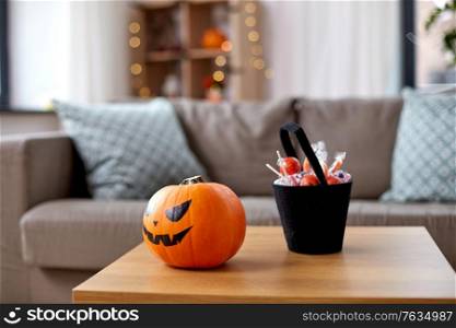 holidays, halloween and party concept - jack-o-lantern pumpkin and candies on wooden table at home. jack-o-lantern and candies at home on halloween