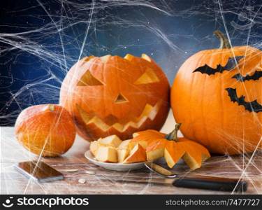 holidays, halloween and technology concept - jack-o-lantern or carved pumpkin, smartphone, knife on wooden table and spiderweb over starry night sky background. halloween jack-o-lantern, pumpkins and smartphone