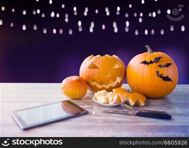 holidays, halloween and technology concept - jack-o-lantern or carved pumpkin with tablet pc computer and knife on wooden table over ultra violet background. halloween jack-o-lantern, pumpkins and tablet pc