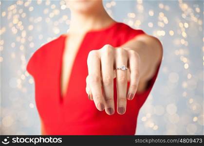 holidays, jewelry and people concept - close up of woman showing engagement ring on her hand over lights background