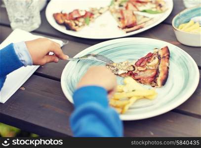 holidays, junk food, dinner, children and people concept - close up of child hands with fork and plate eating pizza at table in summer garden
