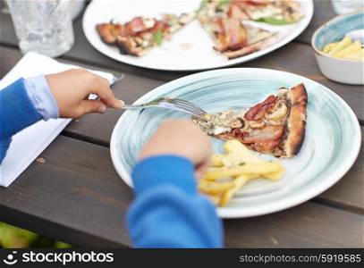 holidays, junk food, dinner, children and people concept - close up of child hands with fork and plate eating pizza at table in summer garden