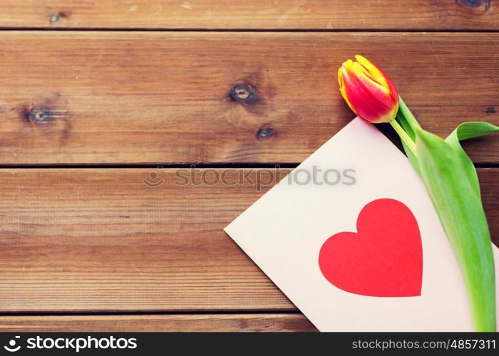 holidays, love and valentines day concept - close up of tulip flowers and greeting card with heart on wooden table