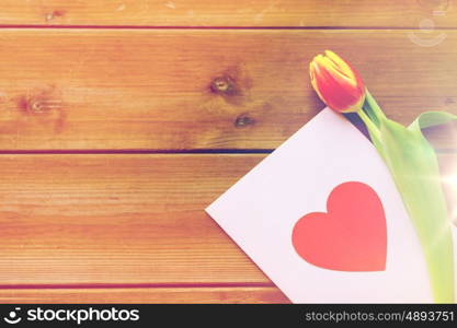 holidays, love and valentines day concept - close up of tulip flowers and greeting card with heart on wooden table