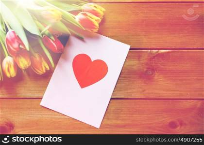 holidays, love and valentines day concept - close up of tulip flowers and greeting card with heart on wooden table. close up of flowers and greeting card with heart