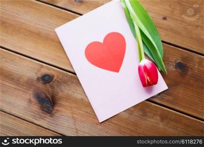 holidays, love and valentines day concept - close up of tulip flowers and greeting card with heart on wooden table