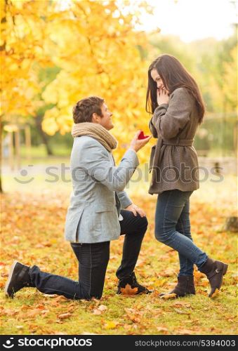 holidays, love, couple, relationship and dating concept - kneeled man proposing to a woman in the autumn park