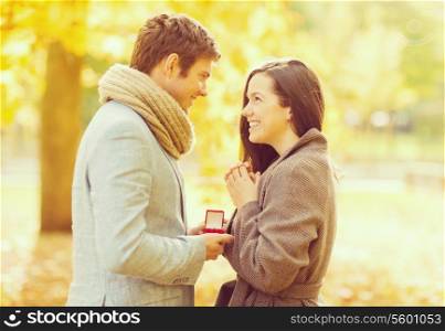 holidays, love, couple, relationship and dating concept - romantic man proposing to a woman in the autumn park