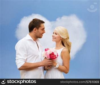 holidays, love, people and dating concept - happy couple with bunch of flowers over blue sky and heart shaped cloud background